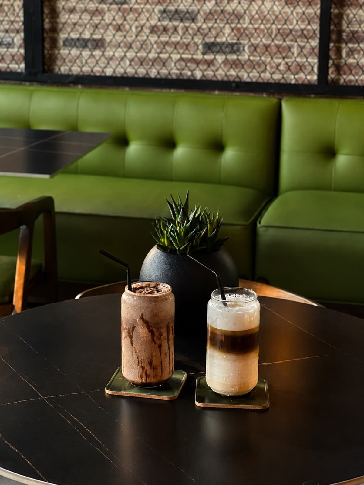 Two iced coffees on coasters in front of a green banquette